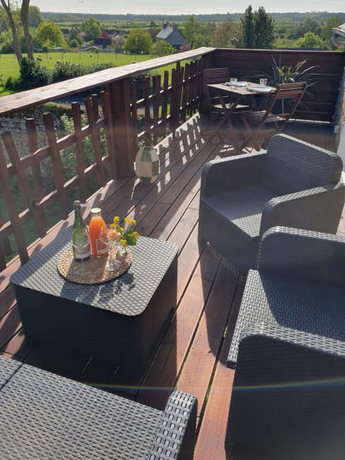 Wooden deck terrace at Le Clos Des Sources with rattan seating, drinks table, and panoramic garden views of Isigny-sur-Mer