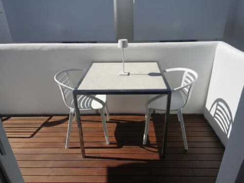 Sala da pranzo moderna a Like at Home Palau con tavolo quadrato, sedie bianche e terrazza in legno che domina pareti grigie