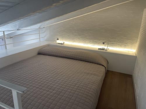 Camera da letto loft moderna presso Like at Home Palau con biancheria trapuntata, pannelli murali testurizzati e illuminazione ambientale calda