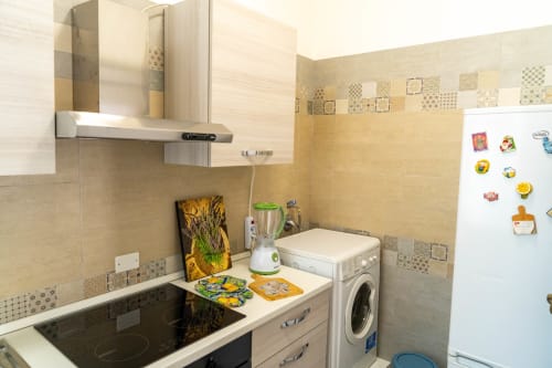 Modern kitchen in Catania apartment with washer, stove, blender, and patterned tile backsplash
