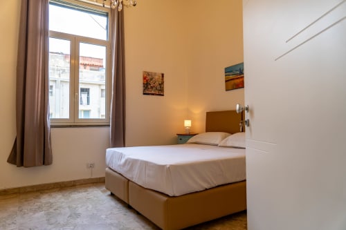 Bright bedroom in Sicily In Home apartment, Catania, with queen bed, window overlooking city, and warm wall tones