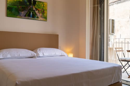 Bright bedroom in Sicily In Home apartment with white bedding, brown headboard, balcony view, and city scenery in Catania