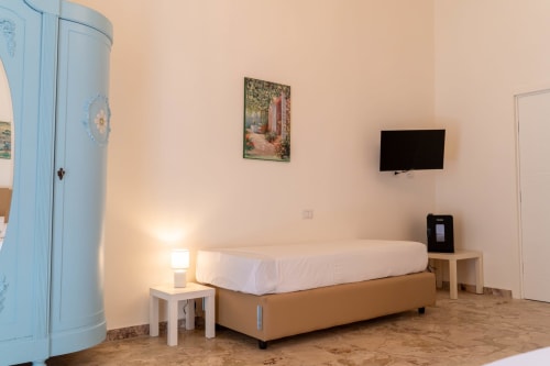Modern bedroom in DOMUS LAVICA apartment, Catania Sicily with bed, flat-screen TV, nightstand lamp, and blue wardrobe