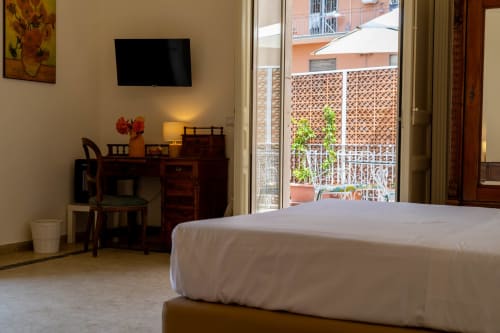 Modern bedroom in Catania apartment with bed, wooden desk, TV, and balcony view of city buildings