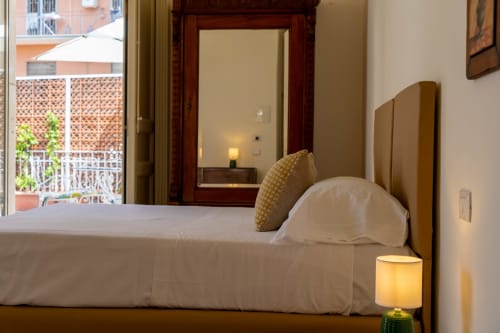Modern bedroom in Catania apartment with city view, white bedding, gold pillow, and terrace access
