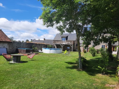 La cour du Clos Des Sources avec piscine, pelouse, chaises longues, arbres et cottages en pierre à Isigny-sur-Mer