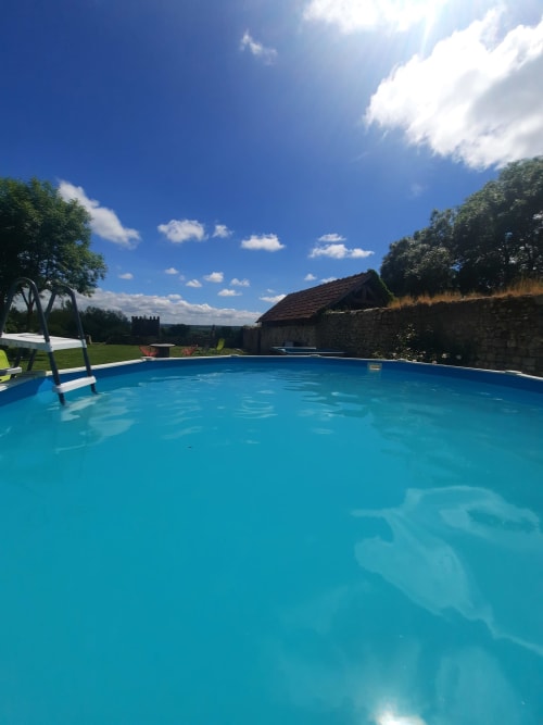 Piscine turquoise du Clos Des Sources à Isigny-sur-Mer avec cottage en pierre et jardin verdoyant sous ciel bleu