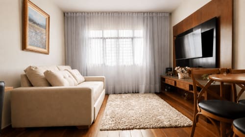 Sala de estar moderna em Goiânia com sofá bege, mesa de madeira, TV inteligente e vista da cidade através de cortinas translúcidas
