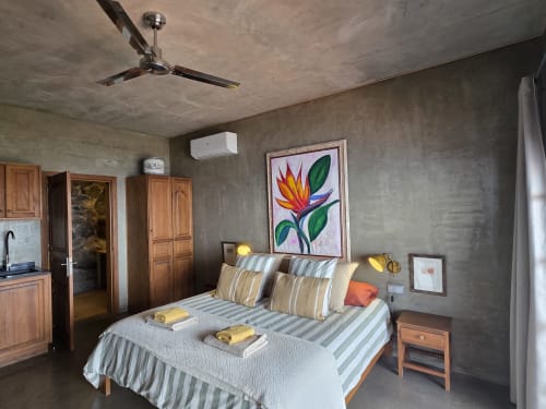 Quarto moderno no Les Terrasses Les Suites em Calheta com roupas de cama listradas, arte colorida e acabamentos em concreto