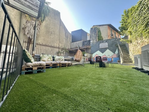 Spacieux jardin de la cour du gîte Ombre de la Tour à Lourdes avec gazon synthétique, mobilier en palettes et tour médiévale