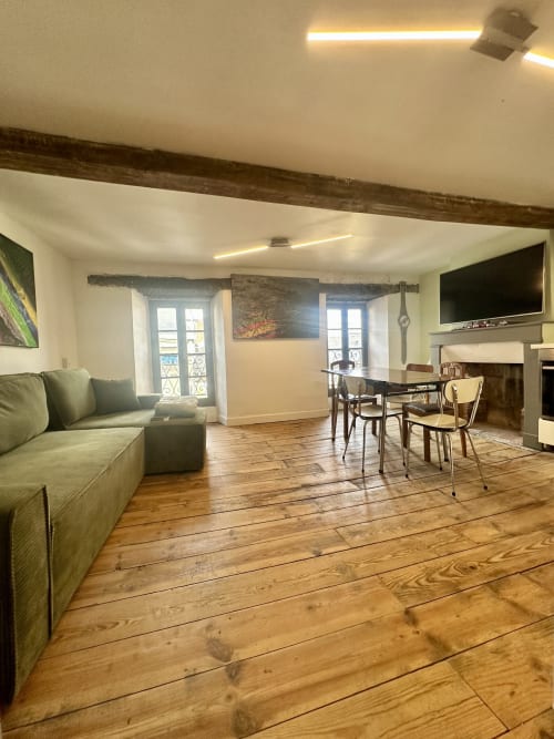 Spacieux séjour de cottage à Lourdes avec poutres en bois, canapé vert, table à manger et vue sur le jardin