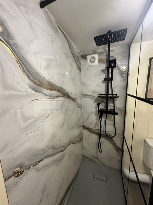 Salle de bain moderne avec pommeau de douche effet pluie noir et carrelage aspect marbre au gîte Ombre de la Tour à Lourdes