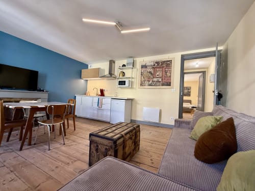 Séjour ouvert à la Maison Lourdes avec table de salle à manger, cuisine, télévision et coins détente aux coussins rayés