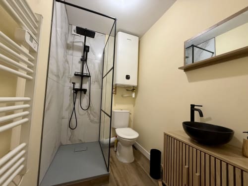 Salle de bain moderne du gîte Ombre de la Tour à Lourdes avec douche spacieuse, vasque noire et sèche-serviettes