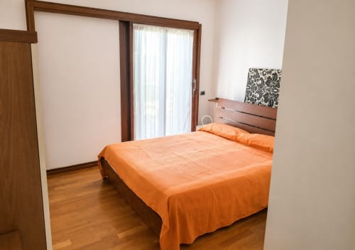 Camera da letto luminosa con biancheria arancione, testata in legno, porte vetrate che si aprono sul balcone, pavimenti in legno a villa Il Nido
