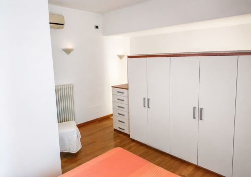 Camera da letto moderna con armadio bianco, pavimento in legno, radiatore e aria condizionata nella villa Il Nido a Treviso