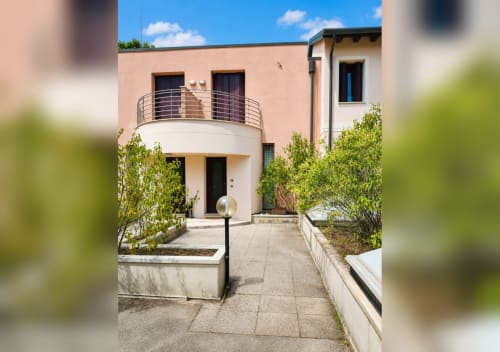 Ingresso della villa Il Nido a Treviso con facciata bianca curva, balcone in metallo, cortile pavimentato e piante verdi