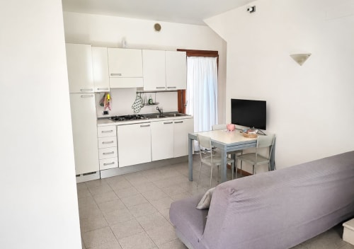 Moderno monolocale a Treviso con cucina bianca, tavolo da pranzo, TV e divano viola nella zona soggiorno