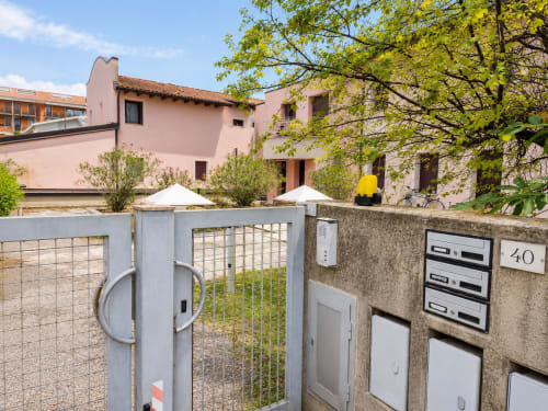 Ingresso della villa rosa con cancello metallico e cassette postali a Il Nido a Treviso, Italia, circondata da vegetazione verde