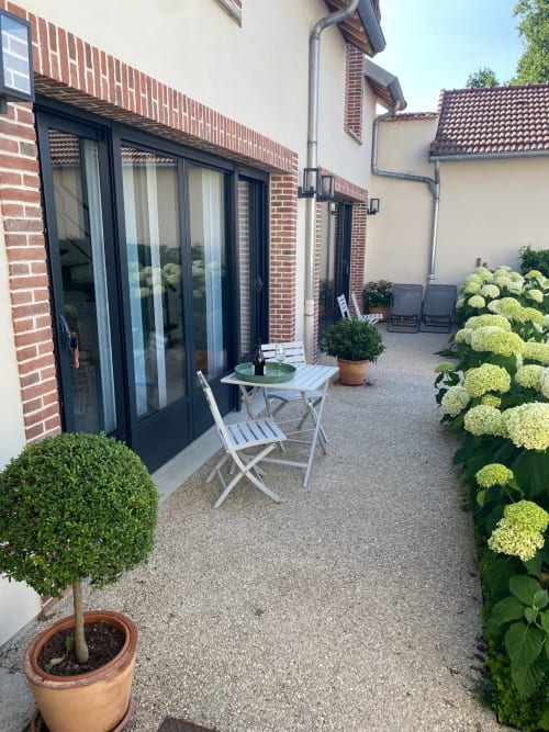 Cour de charme à La Cour Tellier : mobilier blanc, fleurs en pots et façade en brique