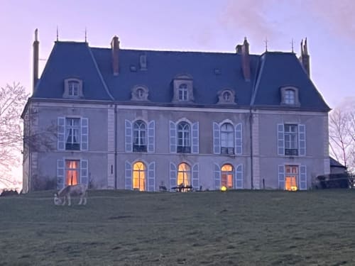 Château de Vaux Morvan illuminé au crépuscule à Étang-sur-Arroux - élégante demeure en pierre avec toit mansardé et façade lumineuse