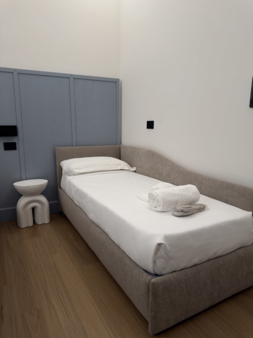 Camera Riviera Deluxe presso Maison Riviera, Reggio di Calabria. Letto singolo con testata imbottita beige, biancheria bianca e cuscini