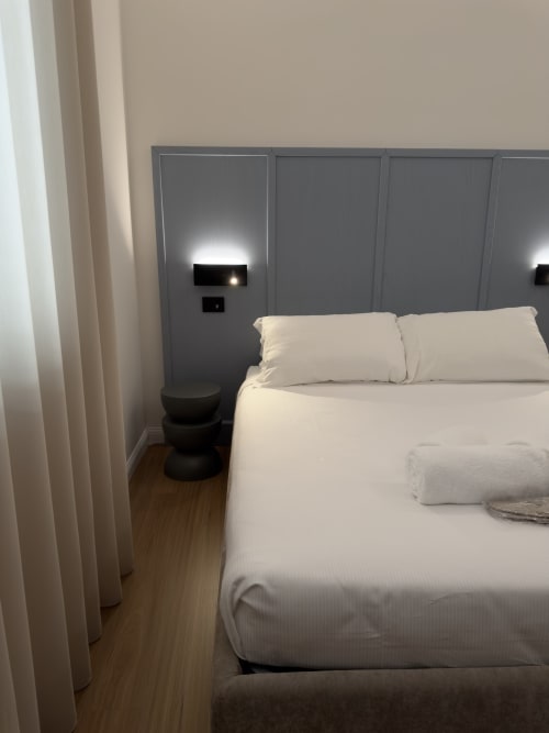 Camera moderna a Maison Riviera con biancheria bianca, testata grigia, pavimento in legno e illuminazione d'accento a Reggio di Calabria