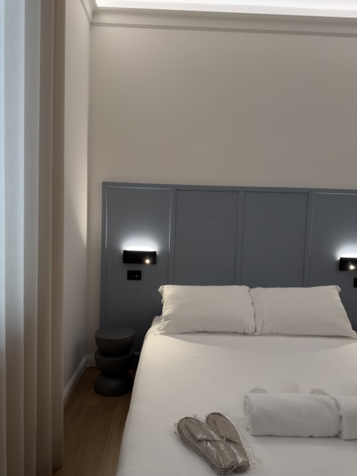 Camera moderna a Maison Riviera con biancheria bianca, testiera scura, luci lettura e pavimento in legno a Reggio di Calabria