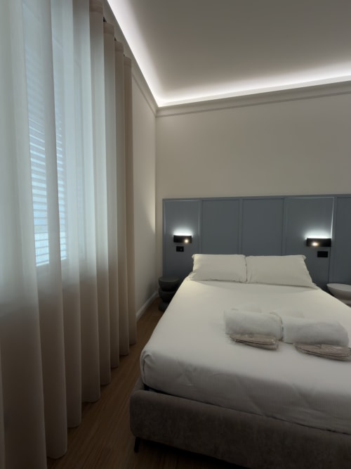 Camera moderna a Maison Riviera con biancheria bianca, testata grigia, illuminazione contemporanea e finestre a tutta altezza