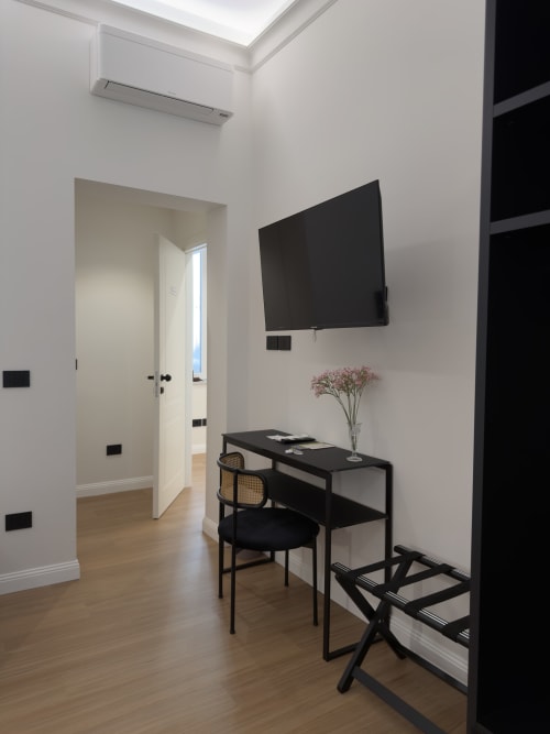 Camera moderna di Maison Riviera con scrivania nera, sedia, TV a parete, fiori e porta aperta a Reggio di Calabria