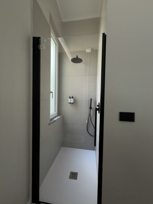 Cabina doccia moderna con porte in vetro nero, soffione a pioggia e piastrelle bianche nella suite di lusso Maison Riviera