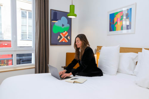 Woman working on laptop in modern hotel room at Hôtel Louvre Richelieu Paris with colorful wall art