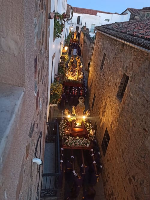 Procesión religiosa por estrechas calles medievales de Cáceres al atardecer, estatuas doradas iluminadas en callejón histórico