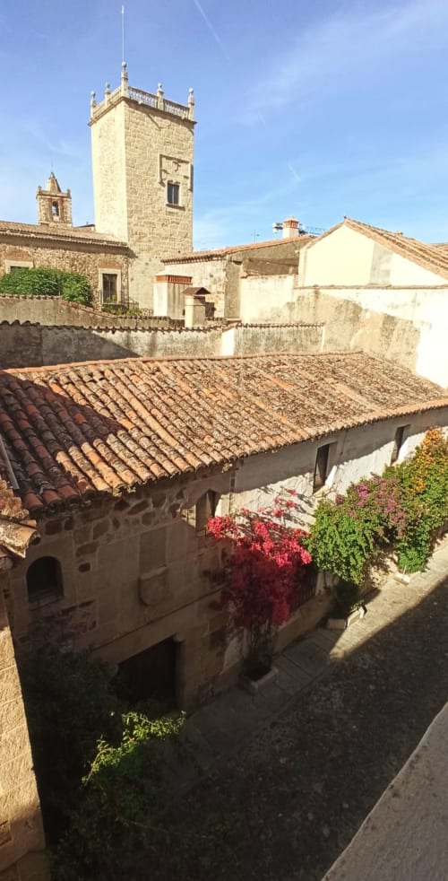 Patio medieval en Mirador Medieval de Cáceres con torre histórica, tejados de barro y muros de piedra cubiertos de hiedra