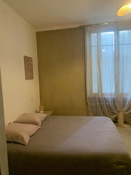 Chambre moderne de l'appartement Mi Casa Es Su Casa à Carcassonne avec lit, mur d'accent olive et fenêtres avec vue sur la ville