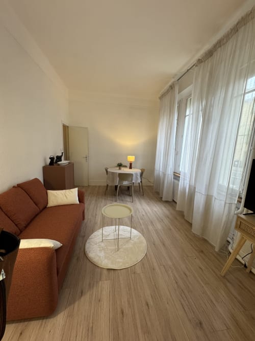Studio moderne à Carcassonne avec canapé rouille, table basse ronde et coin repas vue sur la ville