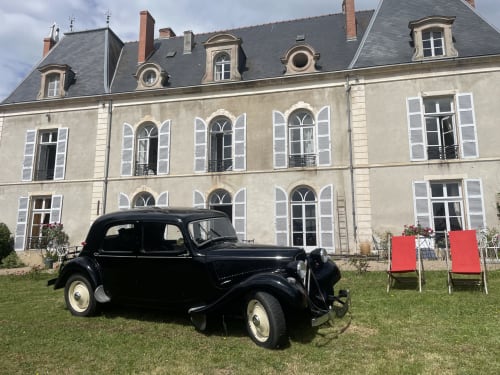 Classic black vintage car parked on lawn in front of elegant stone château with mansard roof in Étang sur Arroux, France