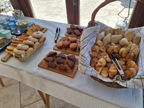 Présentation du buffet petit-déjeuner à La Cour d'Hortense avec viennoiseries, croissants, pains et pâtisseries sur planches en bois
