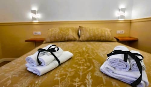 Asciugamani bianchi arrotolati con nastri neri su una coperta dorata in una Suite Tripla Superior presso Vatican Nice Holiday Luxury Rooms
