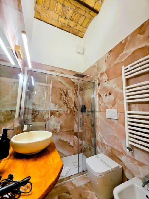 Bagno moderno con piastrelle in marmo marrone, lavabo a bacinella, box doccia in vetro e portasciugamani bianco a Vatican Nice Holiday