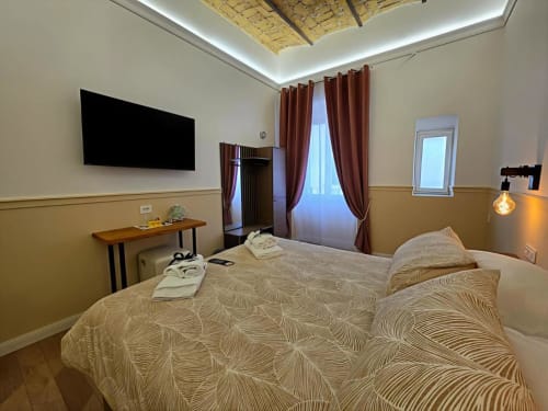 Camera moderna dell'hotel Vatican Nice Holiday Luxury Rooms a Roma con letto, TV a parete, scrivania in legno e tende bordeaux