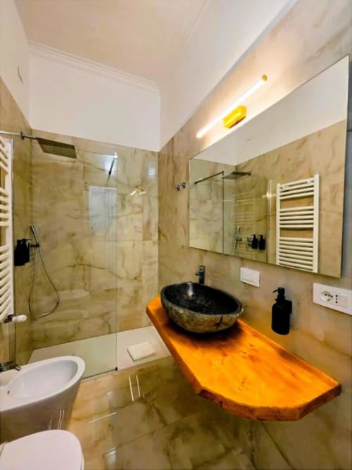 Moderno bagno presso Vatican Nice Holiday Luxury Rooms Roma, con lavabo in pietra nera su mobile legno arancio, piastrelle in marmo