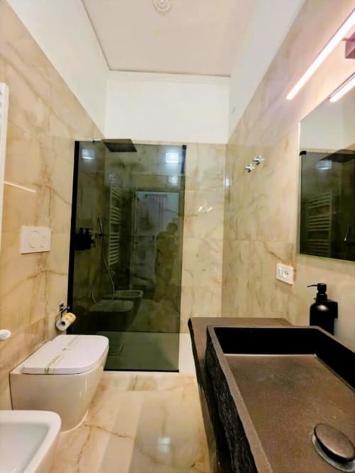 Bagno moderno nel lussuoso hotel Vatican Nice di Roma con pareti in marmo, doccia walk-in, vanità scura e WC