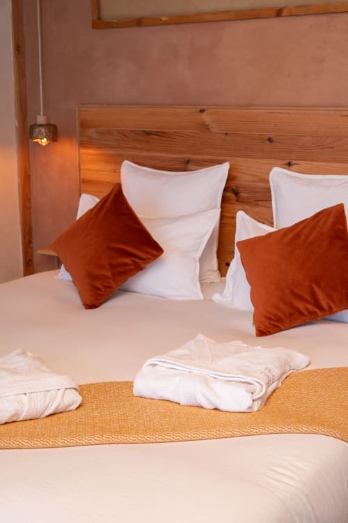 Chambre cosy du Domaine Langelet avec oreillers blancs et couleur rouille, tête de lit en bois et serviettes moelleuses