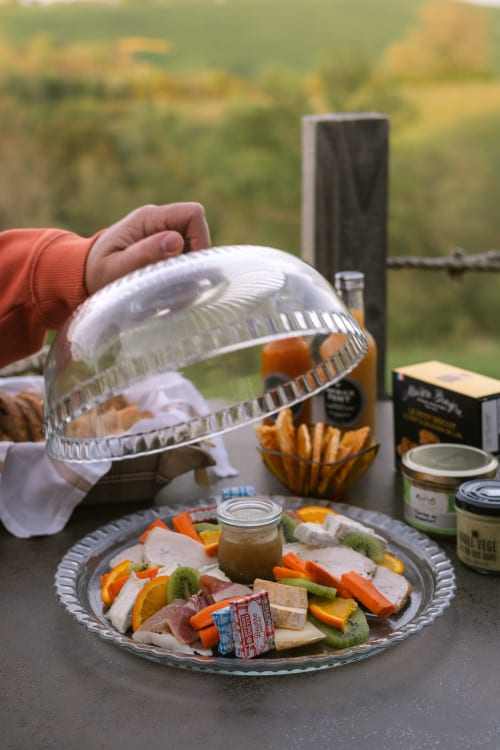 Invité savourant une planche de charcuterie en plein air avec des fruits frais au gîte Domaine Langelet, vue sur la campagne en arrière-plan
