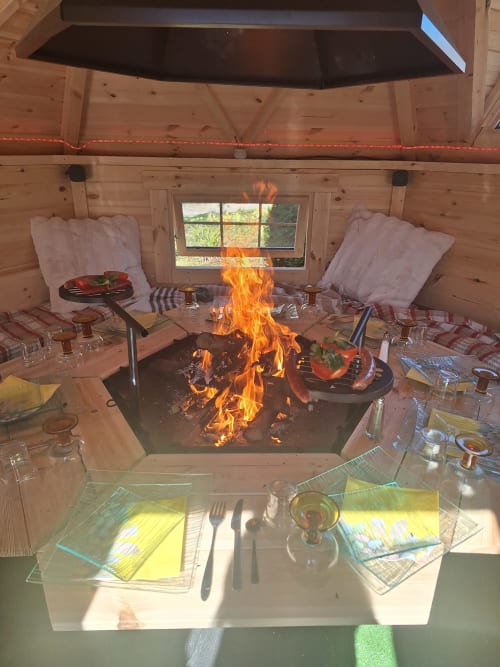 Salle à manger chaleureuse du lodge en bois avec foyer central, table dressée et places confortables à La Cour d'Hortense