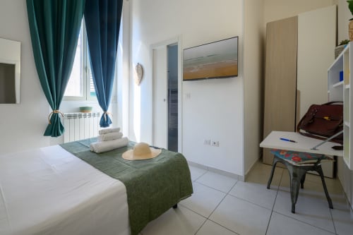 Bright bedroom at Dimore Salentine hotel in Lecce with bed, green accents, desk, window with teal curtains