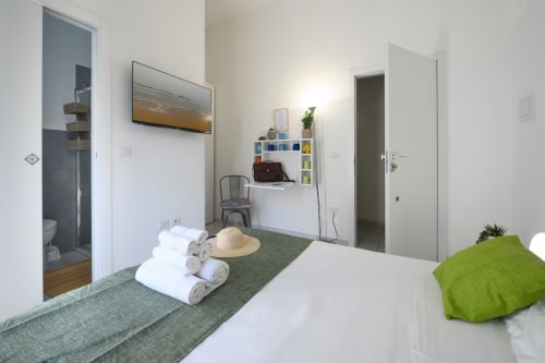 Modern bedroom at Dimore Salentine in Lecce with white bed, green accents, en-suite bathroom and work area with shelving