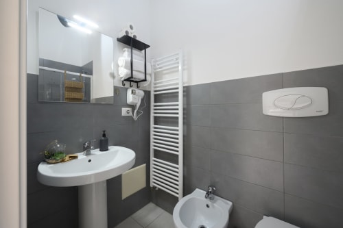 Modern bathroom at Dimore Salentine in Lecce with pedestal sink, bidet, heated towel rack, and gray tile walls