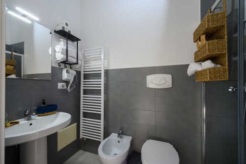 Modern bathroom at Dimore Salentine in Lecce with dark tile walls, white sink, bidet, toilet, heated towel rack, and woven